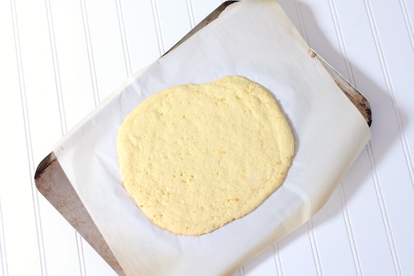 Image, taken from above, shows a cookie sheet covered in parchment paper with low-carb pizza crust dough rolled into an oval.
