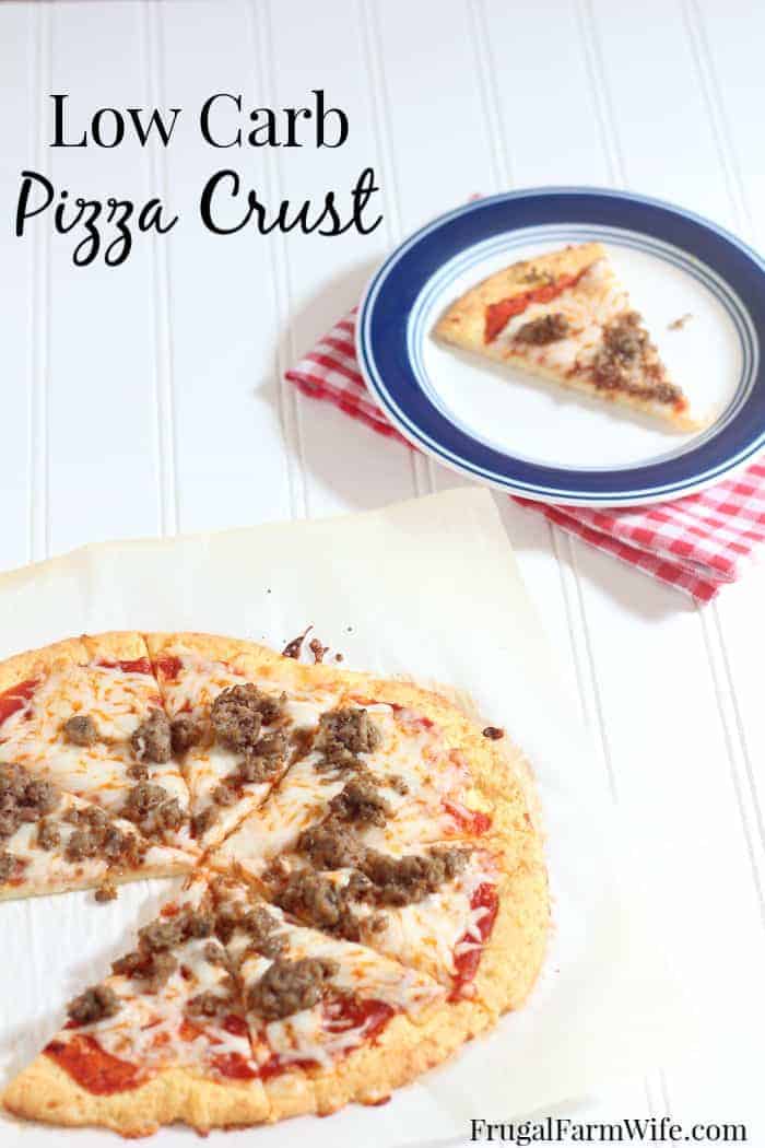 Image shows a white plate with blue trim on a red and white checkered napkin with a piece of pizza on it. The rest of the pizza sits nearby on the table. Text above reads "Low Carb Pizza Crust"