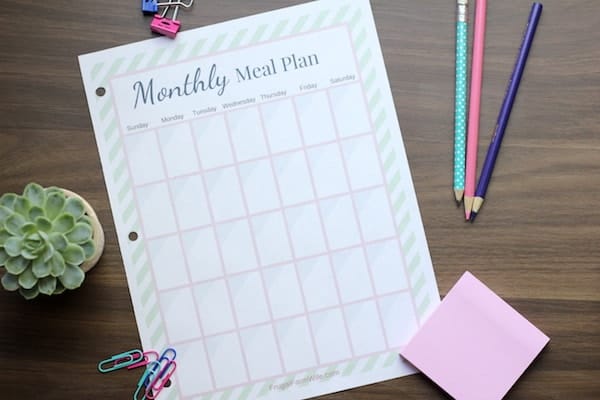 Image, taken from above, shows a sheet of paper with a monthly meal plan printed out, nearby sit pencils, post its, and a small succulent.