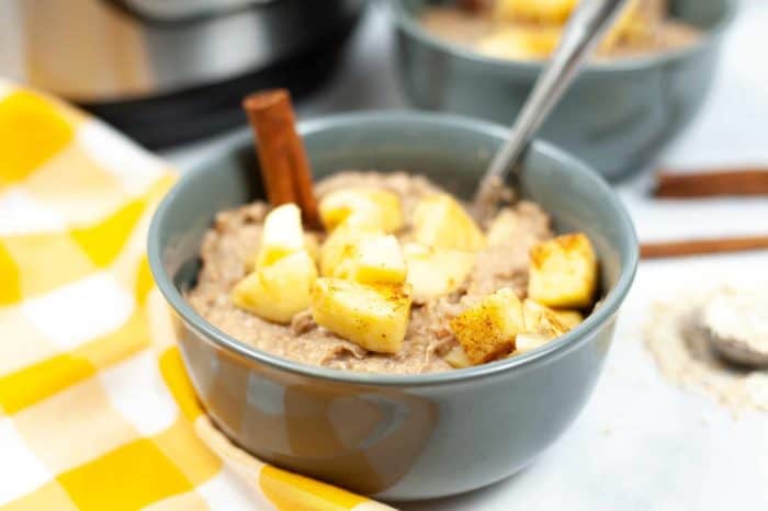 Photo shows a grey bowl of apple cinnamon oatmeal next to a yellow and white checked napkin