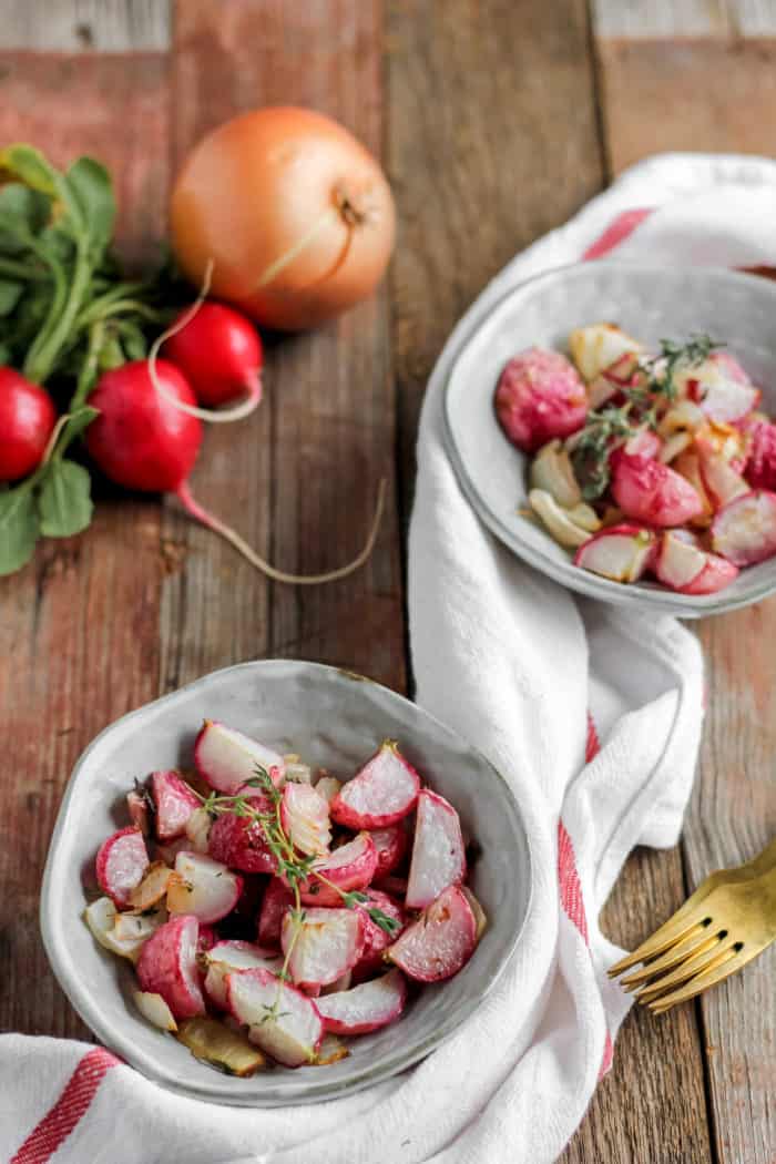 Image shows a table with onion and radishes on it, along with two bowls of roasted radishes