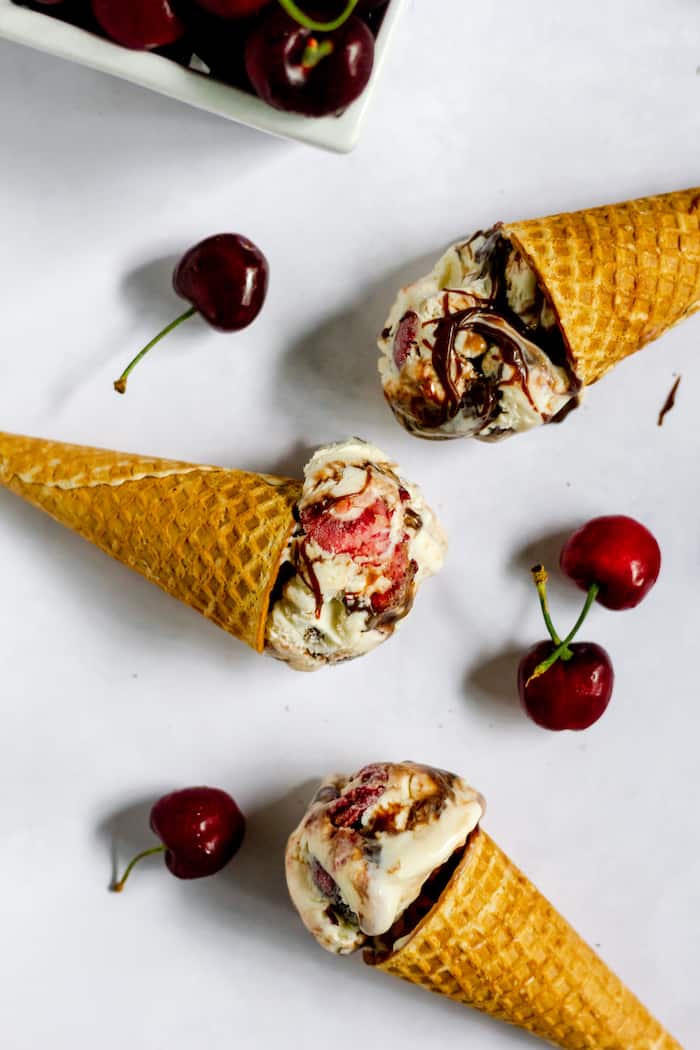 Photo shows several ice cream cones with cherry chocolate ice cream on their sides on a table