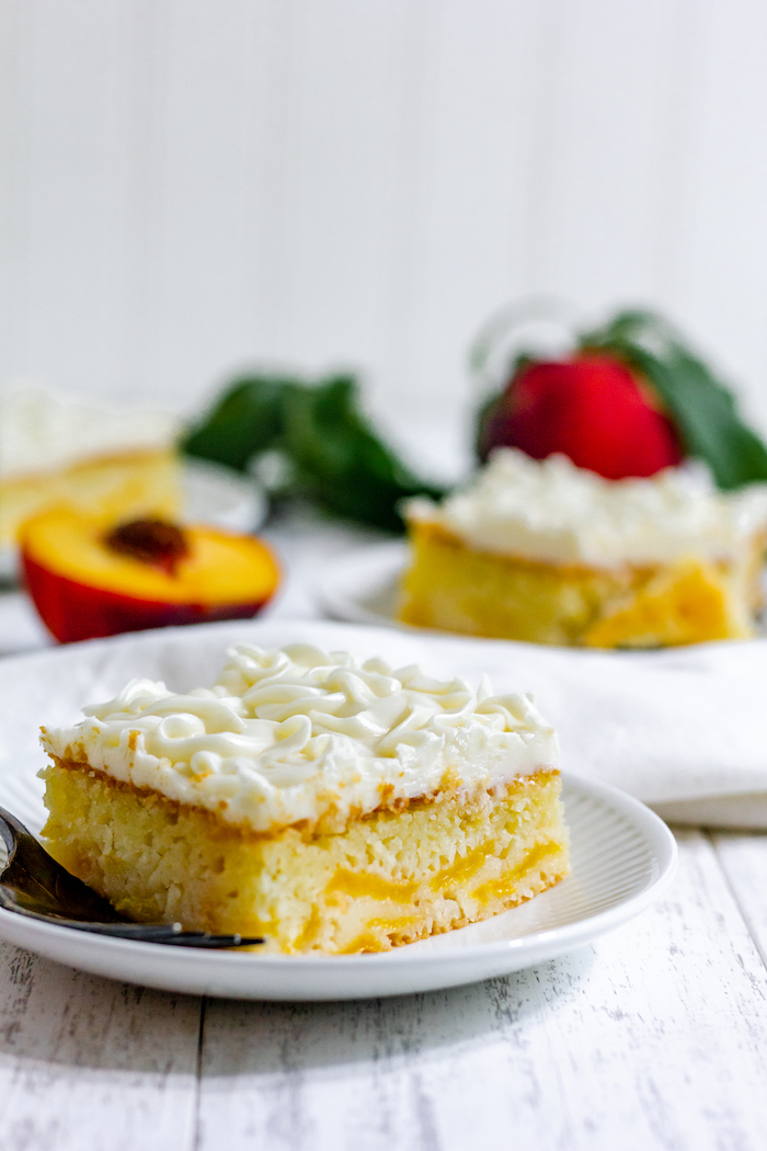 Images shows two slices of peach cake on plates and a white table
