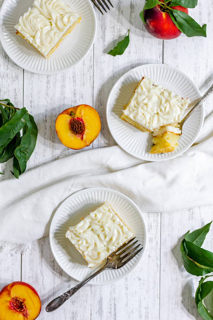 Photo taken from above shows three pieces of peach cake with forks, and a few peaches placed on the table