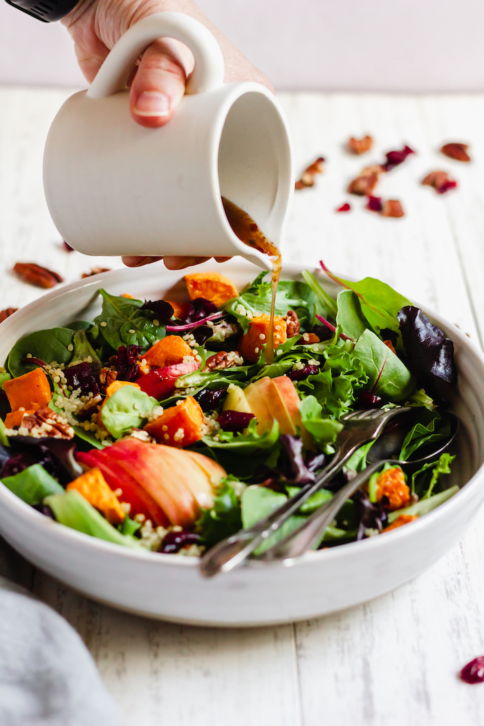 Image shows a mug pouring dressing onto a tasty fall salad