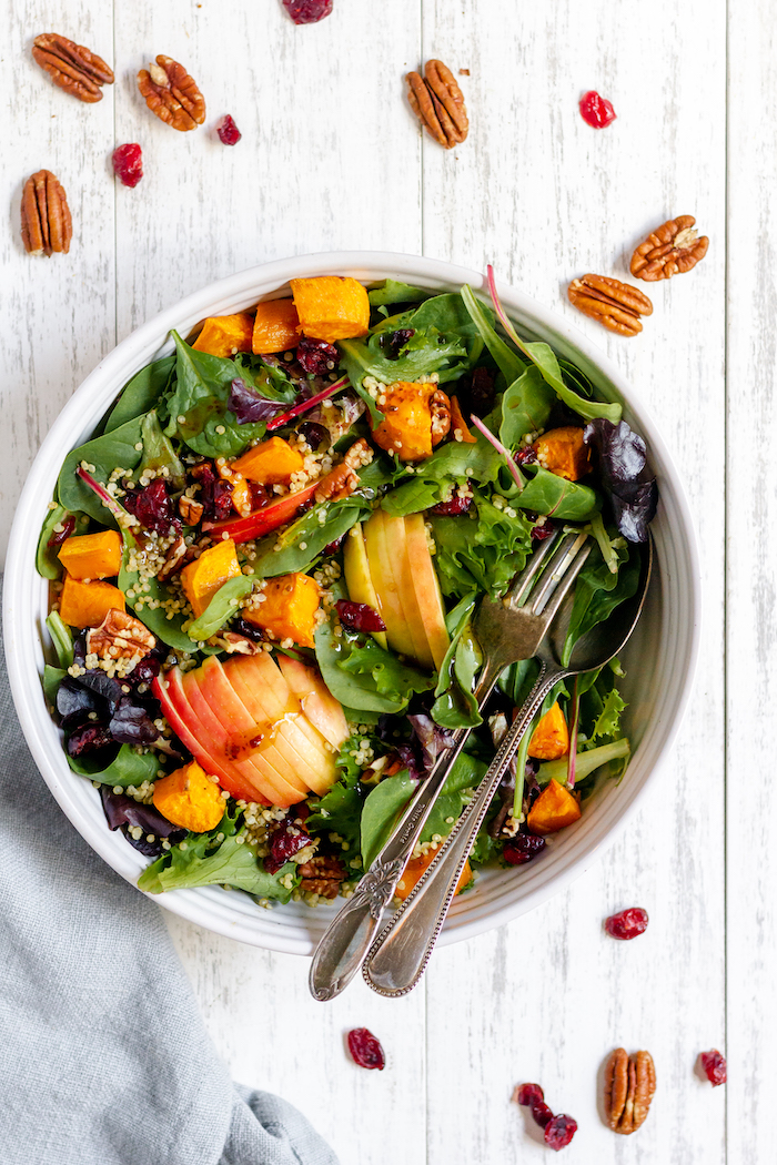 Image shows a colorful green salad photographed from above- with apples, pecans and sweet potatoes