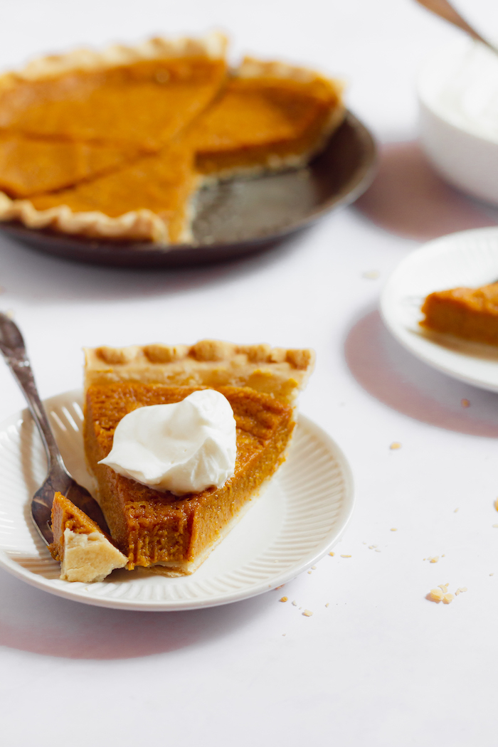 Image shows a slice of sweet potato pie in the foreground, with the rest of the pie in the background