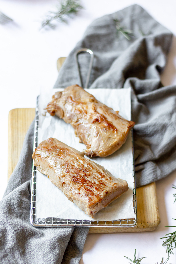 Image shows two pieces of Sous vide pork loin with rosemary on a wire rack with parchment paper.