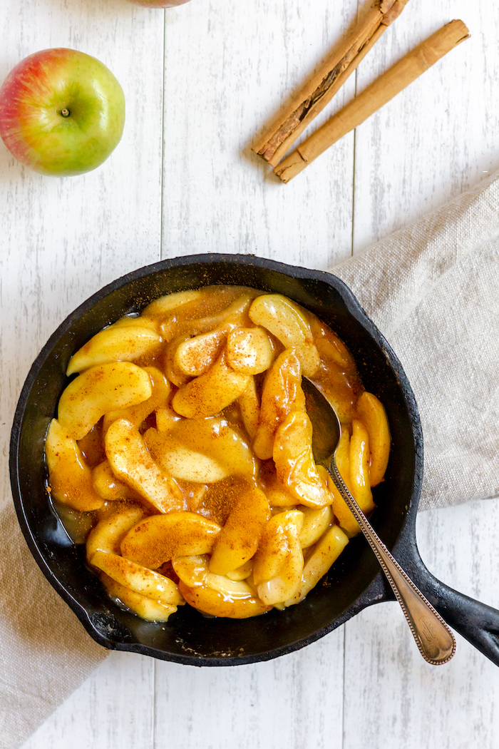 Image shows an iron skillet filled with apple slices
