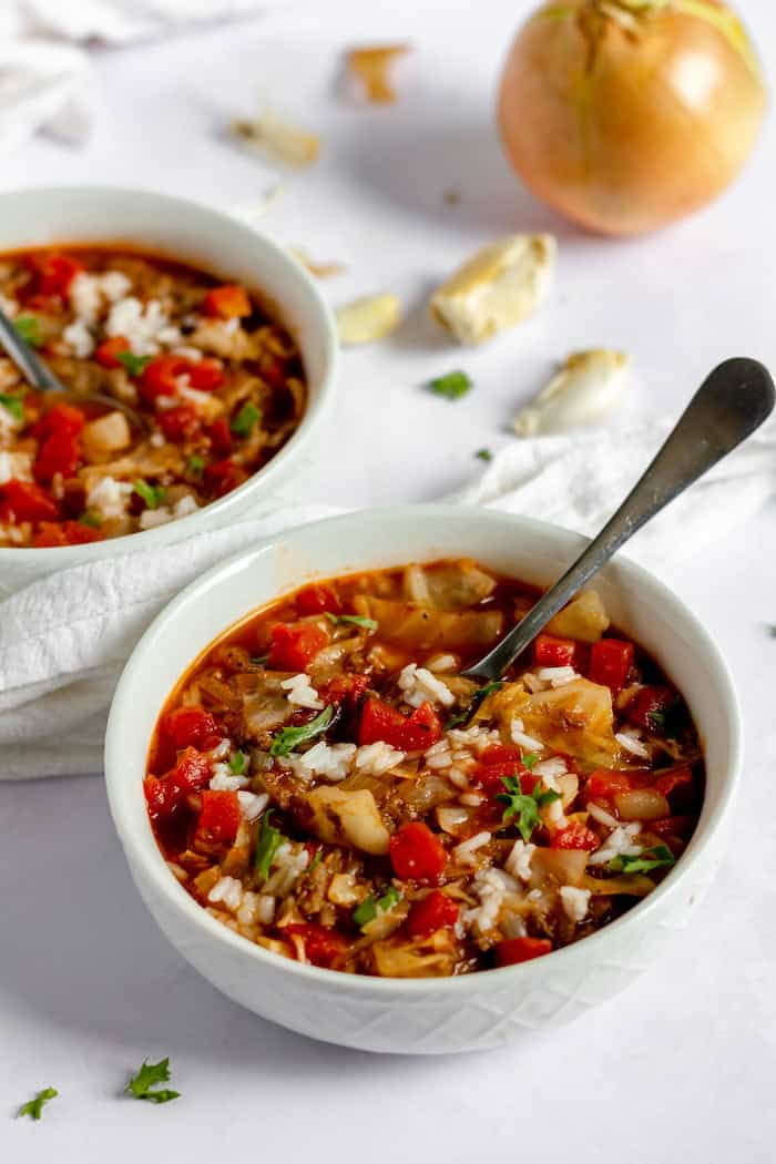 Image shows two white bowls with cabbage soup on a white tablecloth