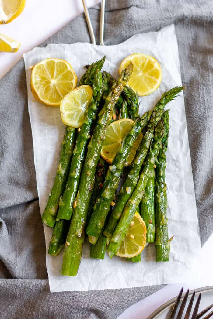 Image shows a parchment paper with stalks of asparagus and lemon rounds on it, resting on a grey towel
