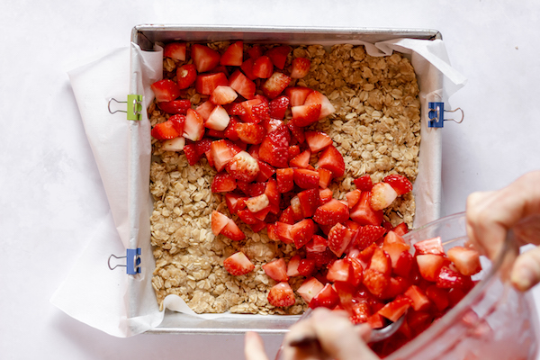 Image, taken from above, shows strawberries being poured into a square pan for baking. 
