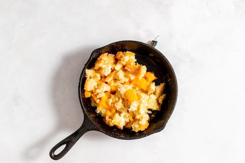 Image, taken from above, shows an iron skillet with crumbled peach cobbler in it for the ice cream.