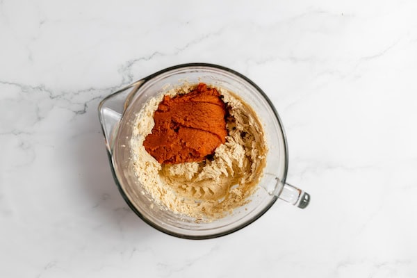 Image, taken from above, shows a mixing bowl with pumpkin in the beaten wet ingredients.