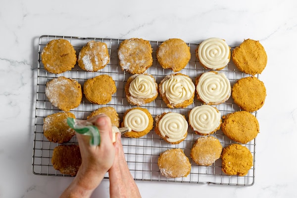 Image, taken from above, shows two hands icing gluten free pumpkin cookies