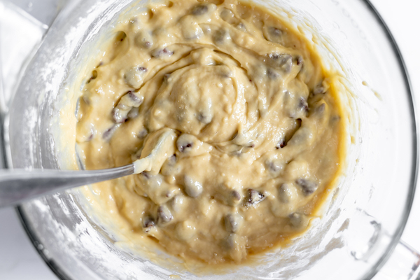 Image, taken from above, shows a spoon in the muffin batter, with chocolate chips stirred into the batter.