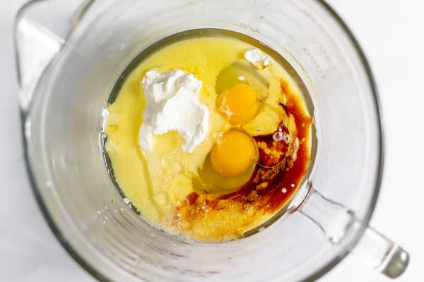 Photo, taken from above, shows a glass mixing bowl with wet ingredients ready to be mixed- oil, egg, vanilla
