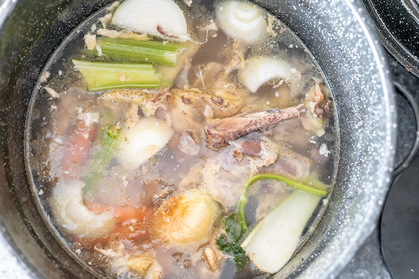 Image, taken from above, shows a large stock pot filled with water, chicken bones and vegetables, ready to make broth.