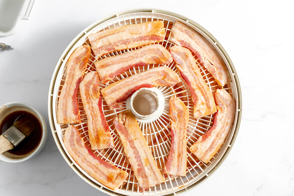 Image, taken from above, shows bacon jerky in a dehydrator on a countertop.