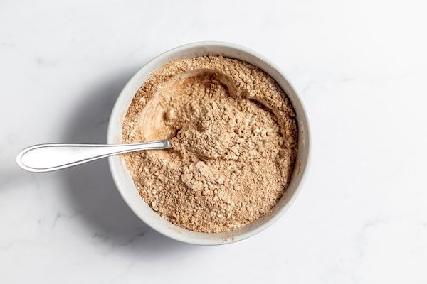 Image, taken from above, shows a white bowl with a spoon in it, full of dry ingredients for gluten free chocolate cupcakes