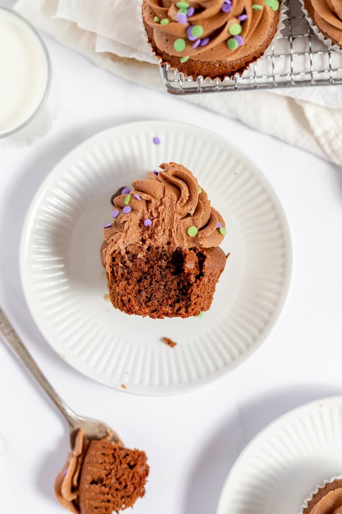 Image, taken from above, shows a gluten free chocolate cupcake sitting on a plate with a bite taken out of it to show the texture of the cake.