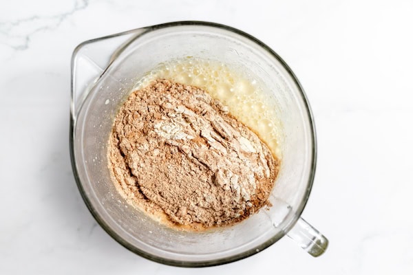 Image, taken from above, shows a large glass mixing bowl with the dry ingredients being added to wet ingredients for gluten free chocolate cupcakes
