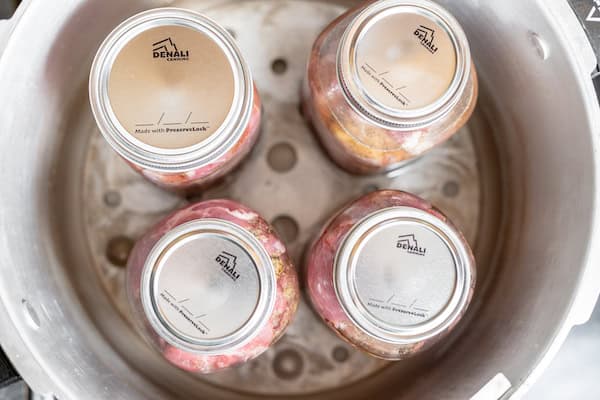 Image, taken from above, shows several jars in a canner to be sealed.