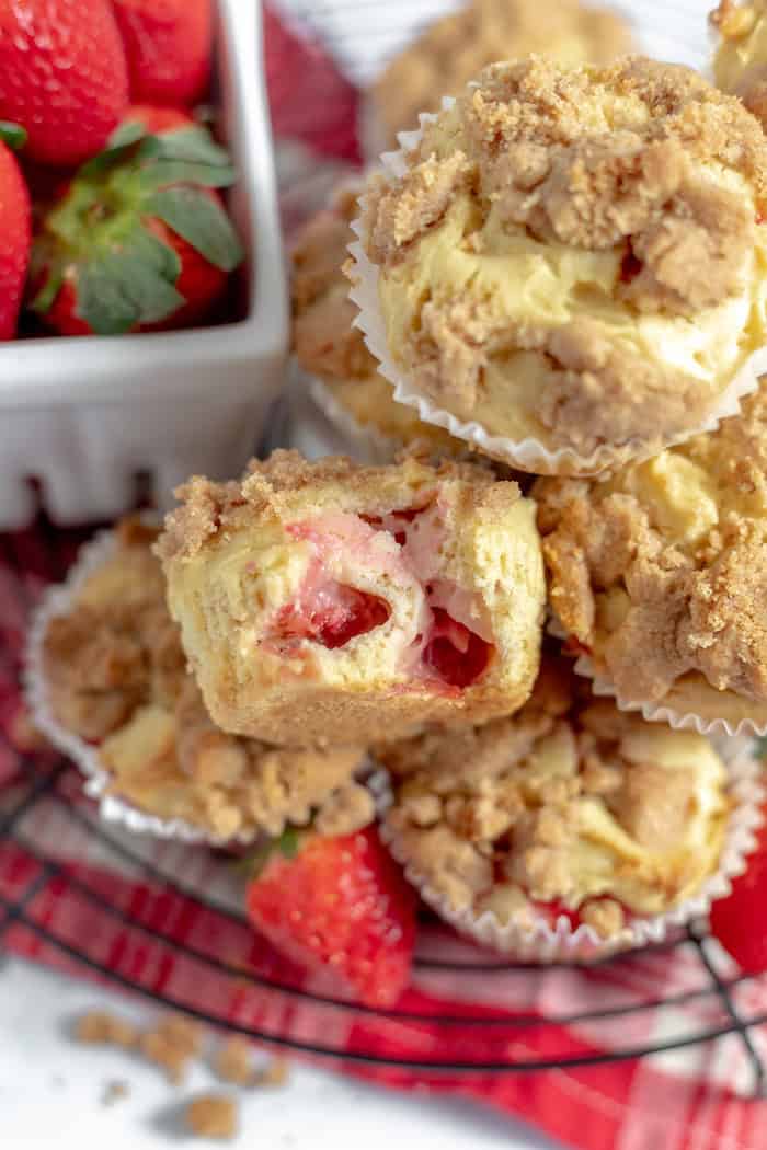 Image shows a close up of gluten free strawberry muffins stacked on one another. the top muffin has a bit taken out of it to show the texture and strawberries inside. 