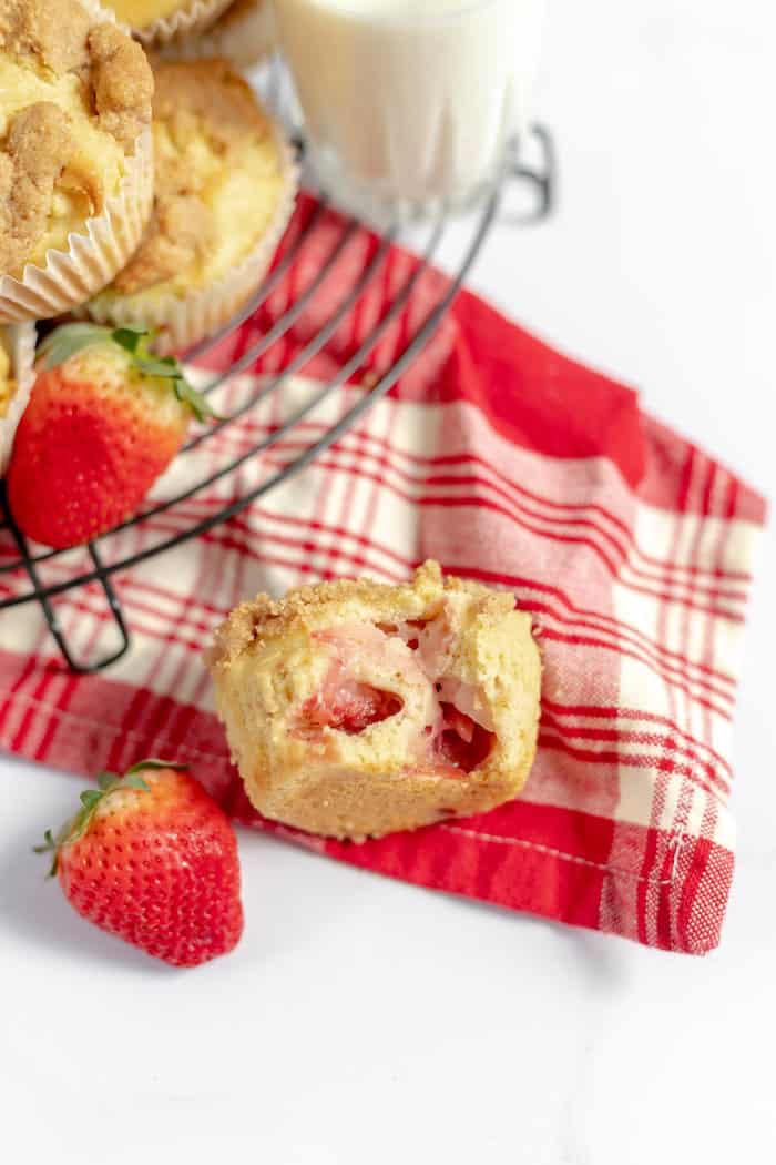 Image shows a red and white towel on a table, with muffins on a cooling rack and a glass of milk