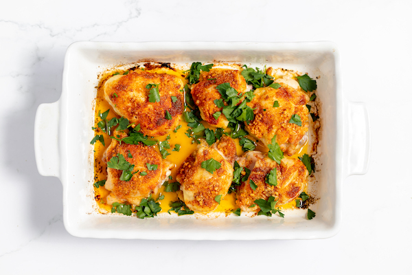 Image, taken from above, shows parsley sprinkled on baked chicken thighs in the casserole dish