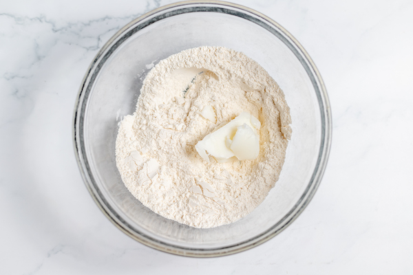 Image, taken from above shows flour, salt, and lard in a glass bowl on a counter top.