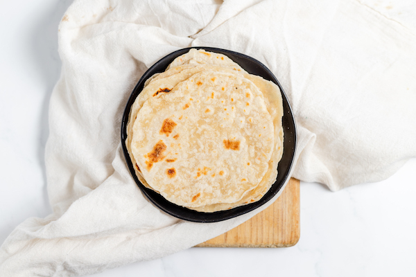 Image shows a stack of homemade sourdough tortillas ready to eat on a wooden cutting board.