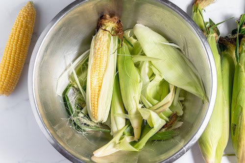 husking sweet corn in a bowl