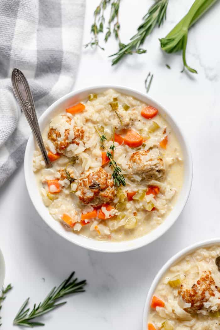 Image, taken from above, shows a bowl of chicken meatballs soup served with herbs on a table.