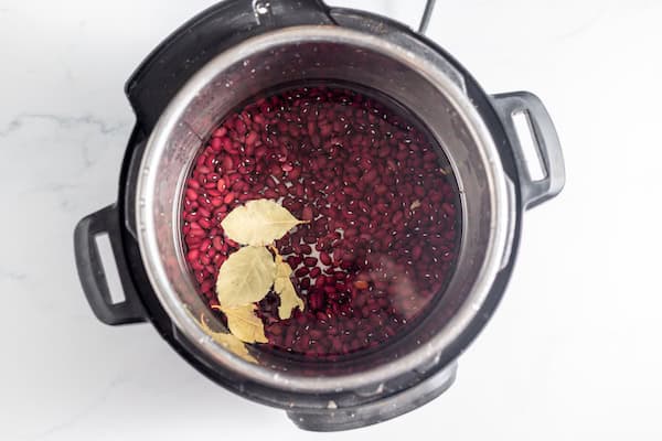 Image, taken from above, shows an Instant Pot with beans cooking with bay leaf.