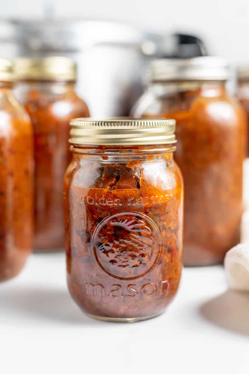 Image shows several jars of home-canned chili on a counter with a pressure canner in the background.