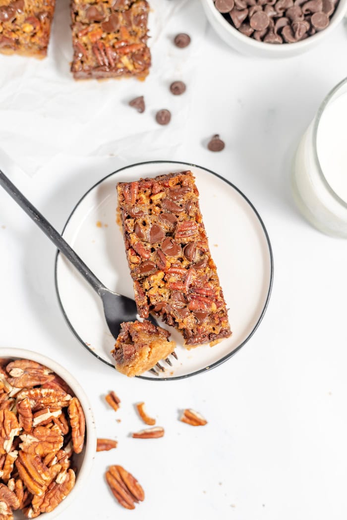 Image, taken from above, shows a piece of the chocolate pecan bar on a place, with a fork and a bite taken from it