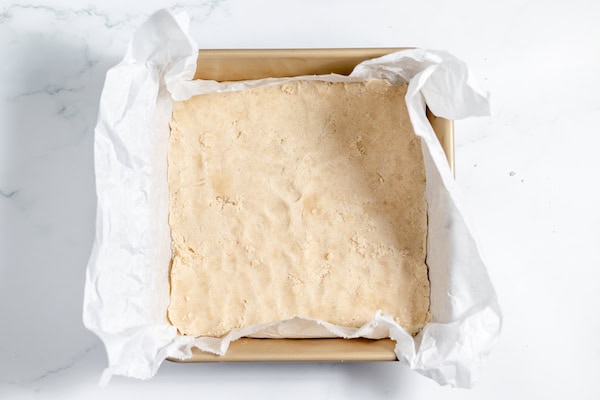 Image, taken from above, shows the crust pressed into the bottom of a pan lined with parchment paper.