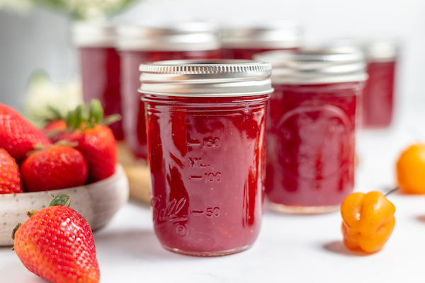 jam in jars with a bowl of strawberries on one side, and habanero peppers on the other