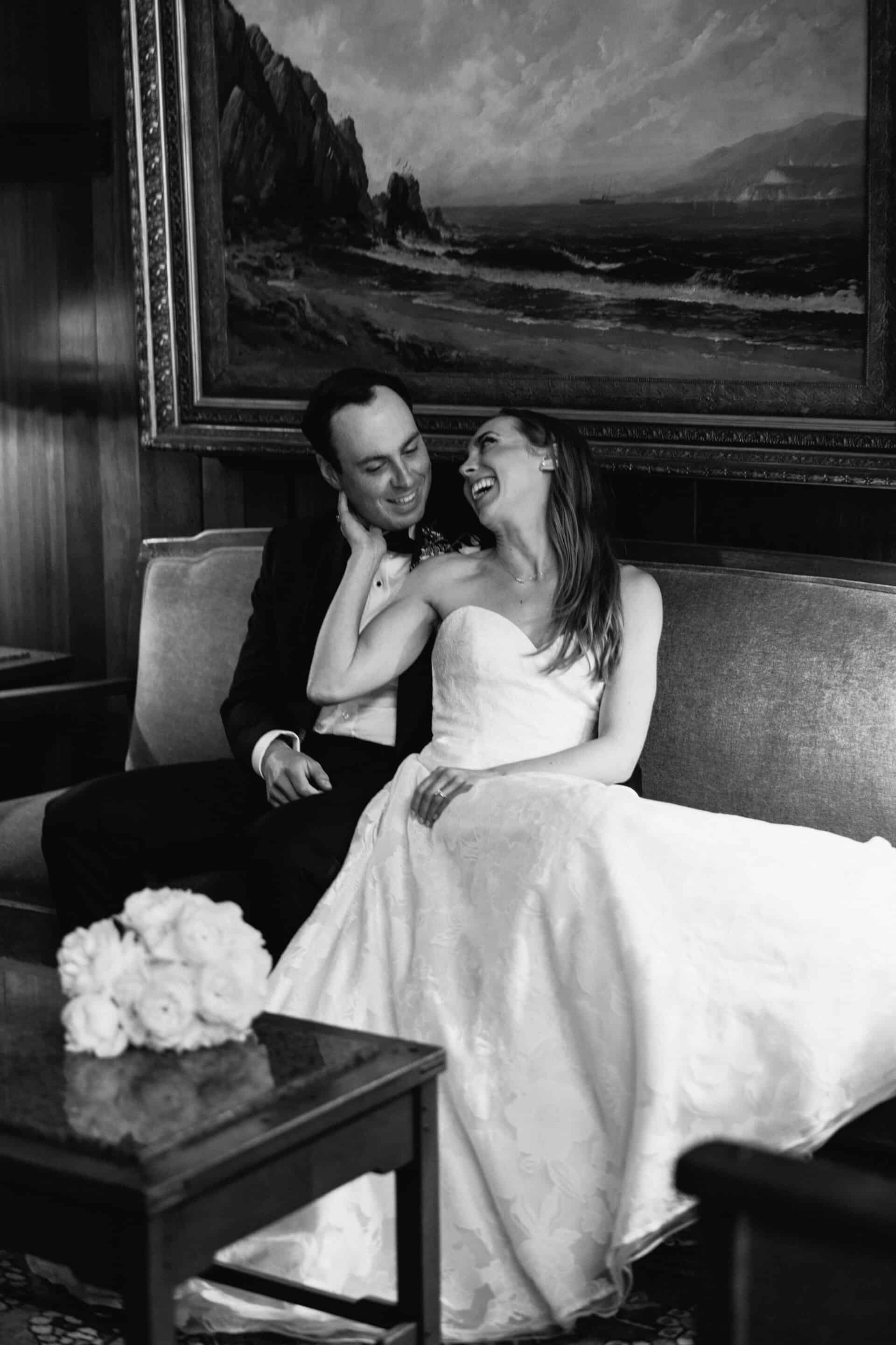 Black and white photo of a bride and groom sharing a joyful moment on their wedding day.