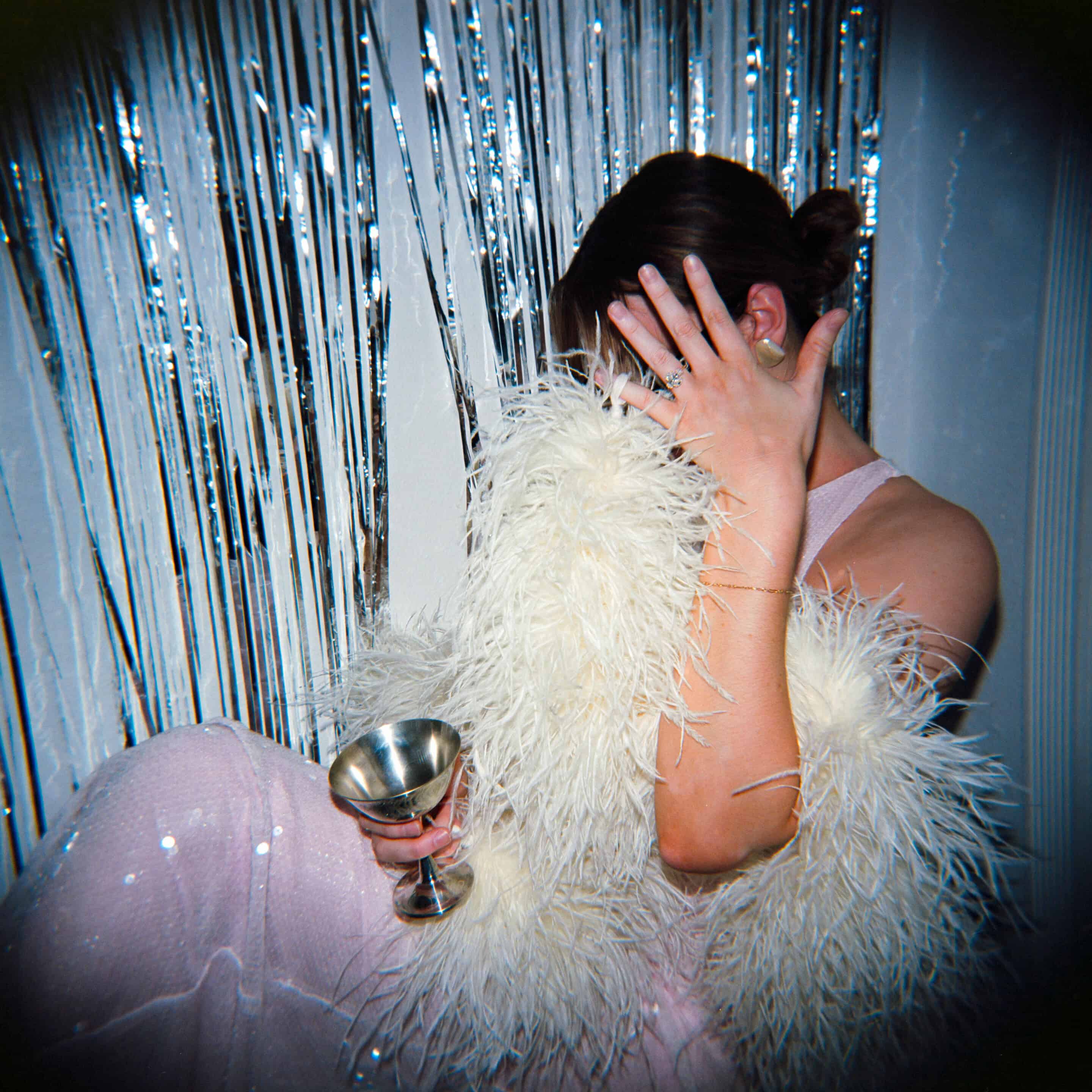 Woman in glamorous outfit with feathered coat and champagne glass at party.