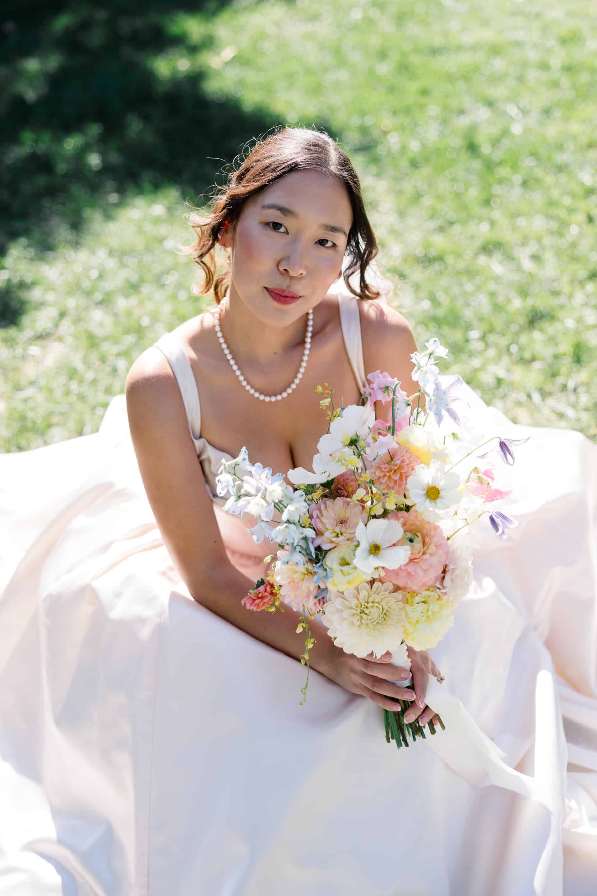 bride sitting on the grass with spring colorful bouquet and pink wedding dress at madonna inn san luis obispo california