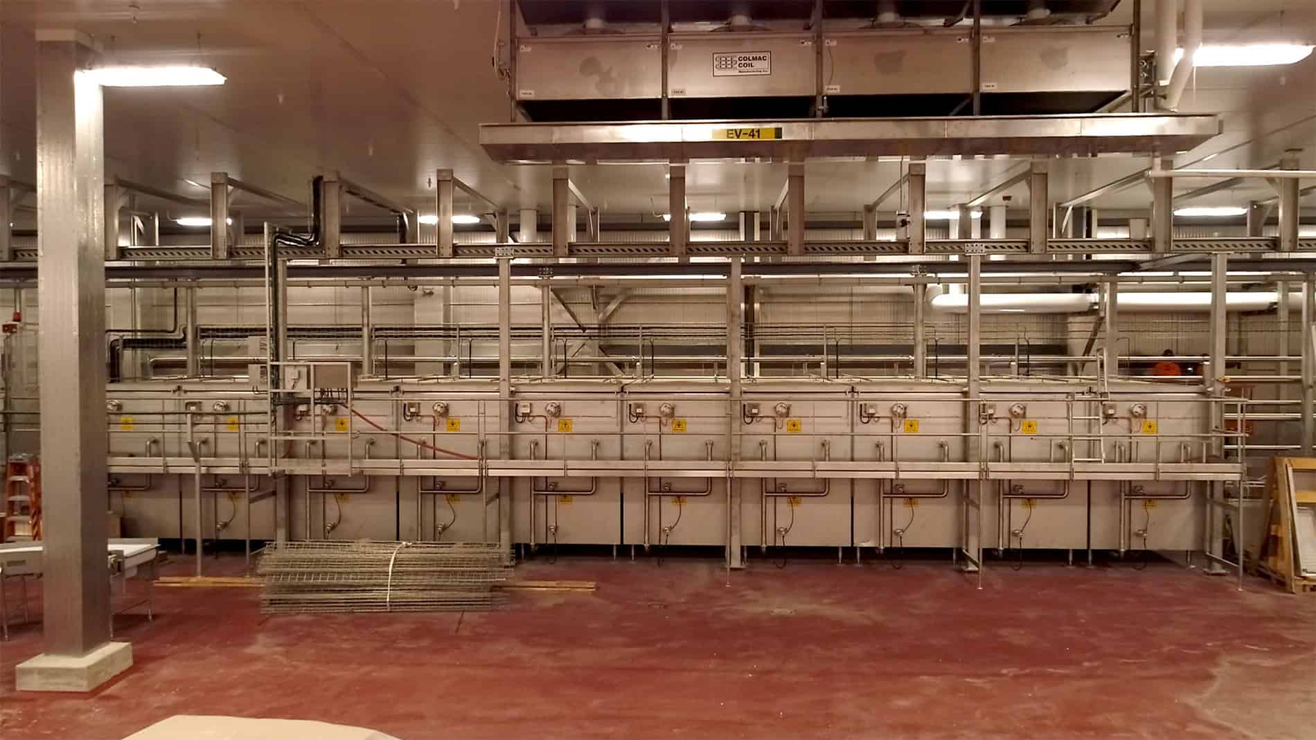 The back wall of the well-lit large room is lined with processing and other equipment on a clean, red concrete floor, part of the Ruprecht Meat Company Processing Facility.