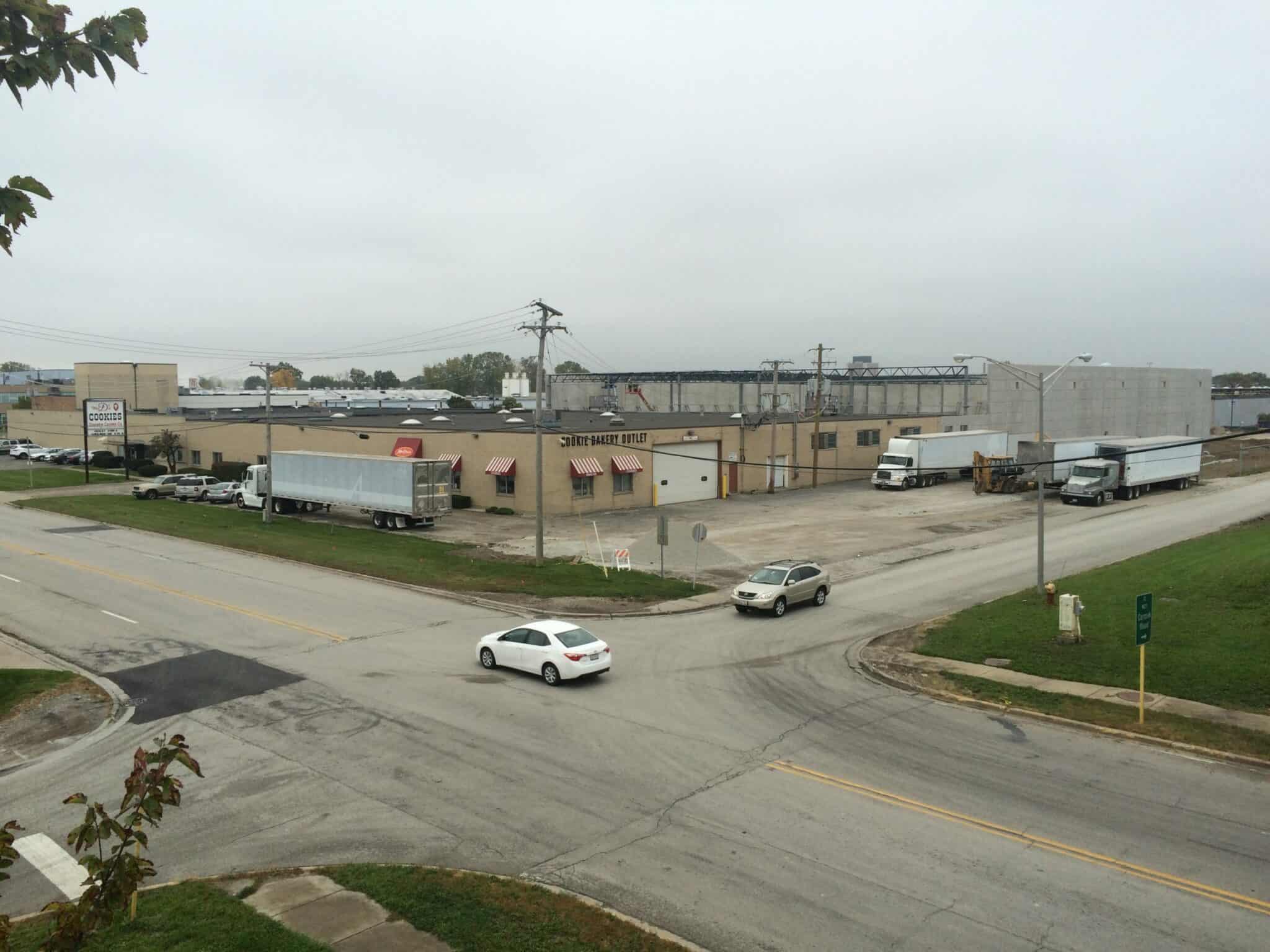 The “before” image of the Pure’s Food facility shows a run-down industrial building with red and white striped awning over the few windows, concrete wall construction on the back of the facility, and trucks parked in the parking lot while cars use the street in front.