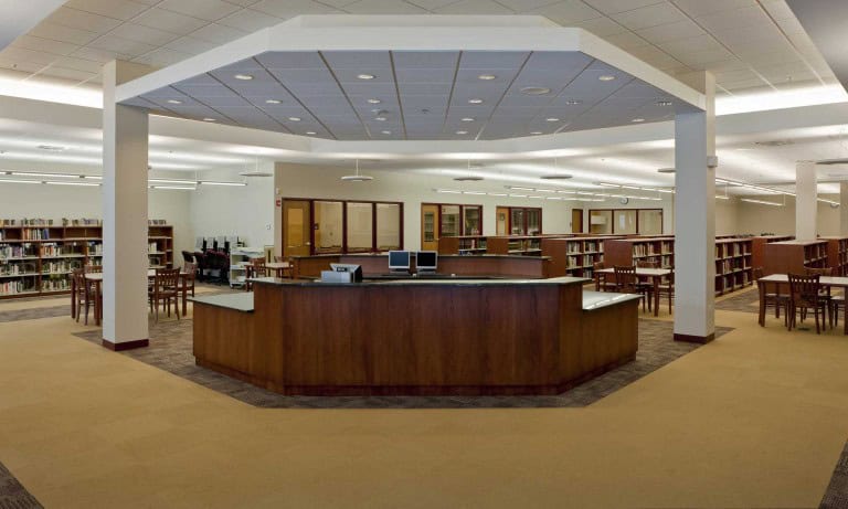 Montini Catholic High School’s library is an open-concept room with a prominent librarian’s desk, low bookshelves, a meeting room, and desks behind the welcome area.
