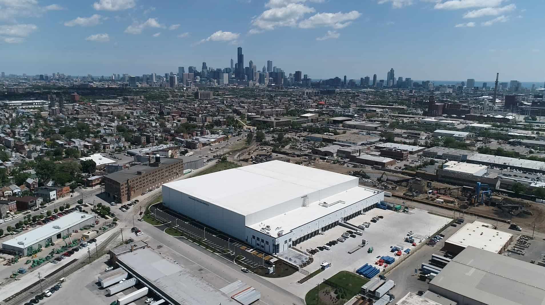 An aerial view of the Preferred Freezer Services #3 facility shows the bright white building centered on a new, clean campus in the foreground of a cityscape.