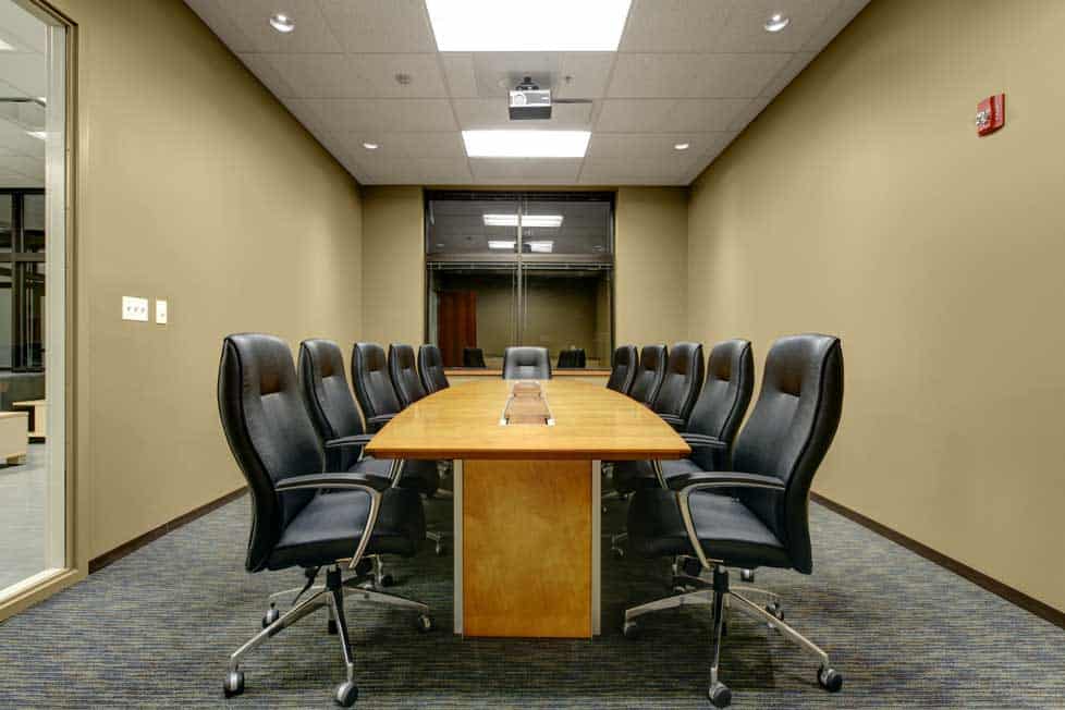 A long table and comfortable chairs sit in a well-lit conference room with light-colored walls and a grey carpet. The Lenze interior was built by Keeley Construction, Inc.