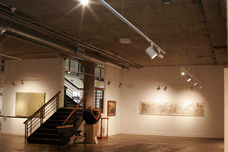 A metal staircase provides access to a warmly lit lower level with art of various kinds prominently displayed on the walls. Keeley Construction, Inc. renovated the National Vietnam Veterans Art Museum.