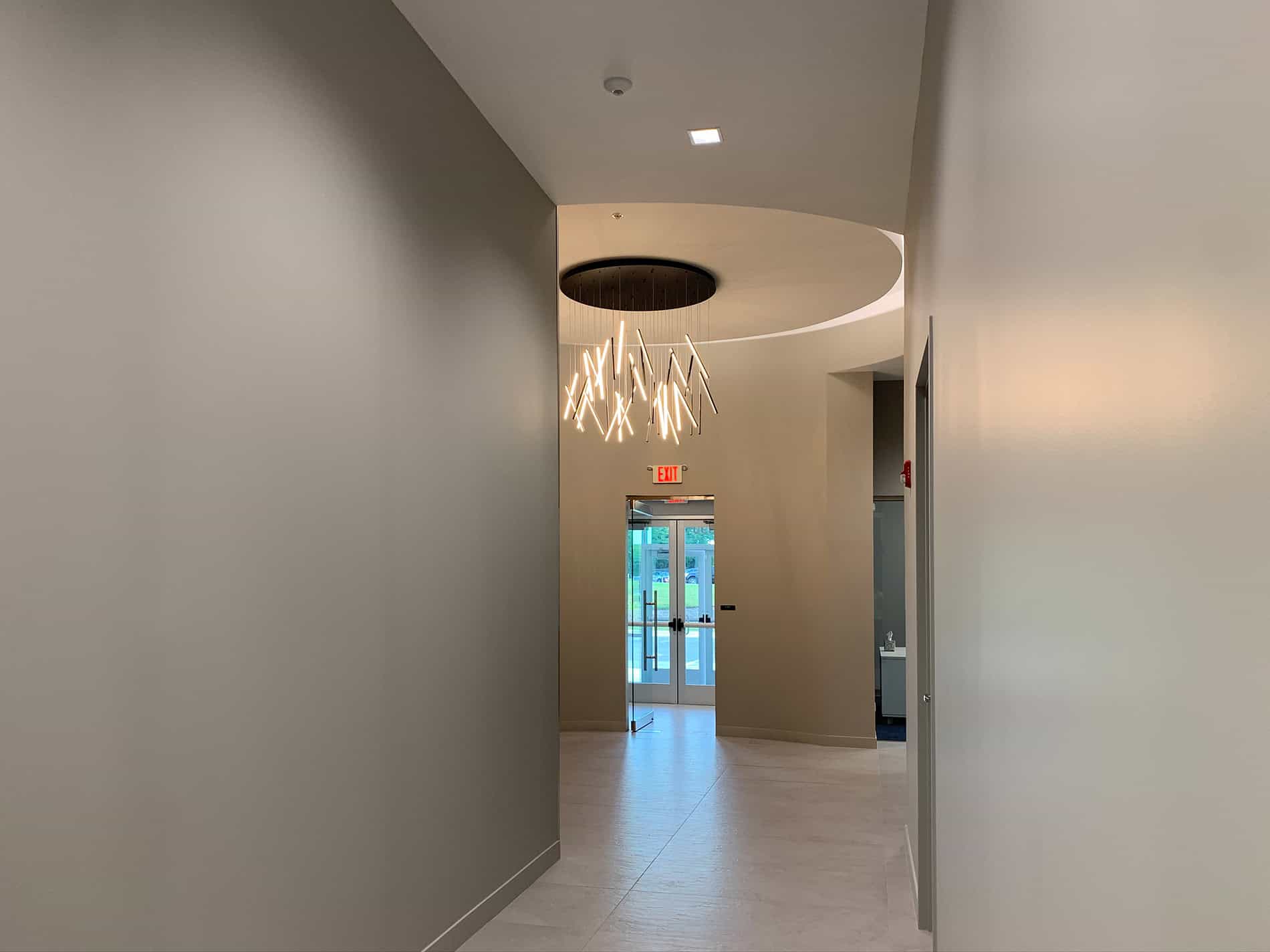 A modern glass chandelier is made of cylinders of lights and hangs in a round entryway at the end of a hall.