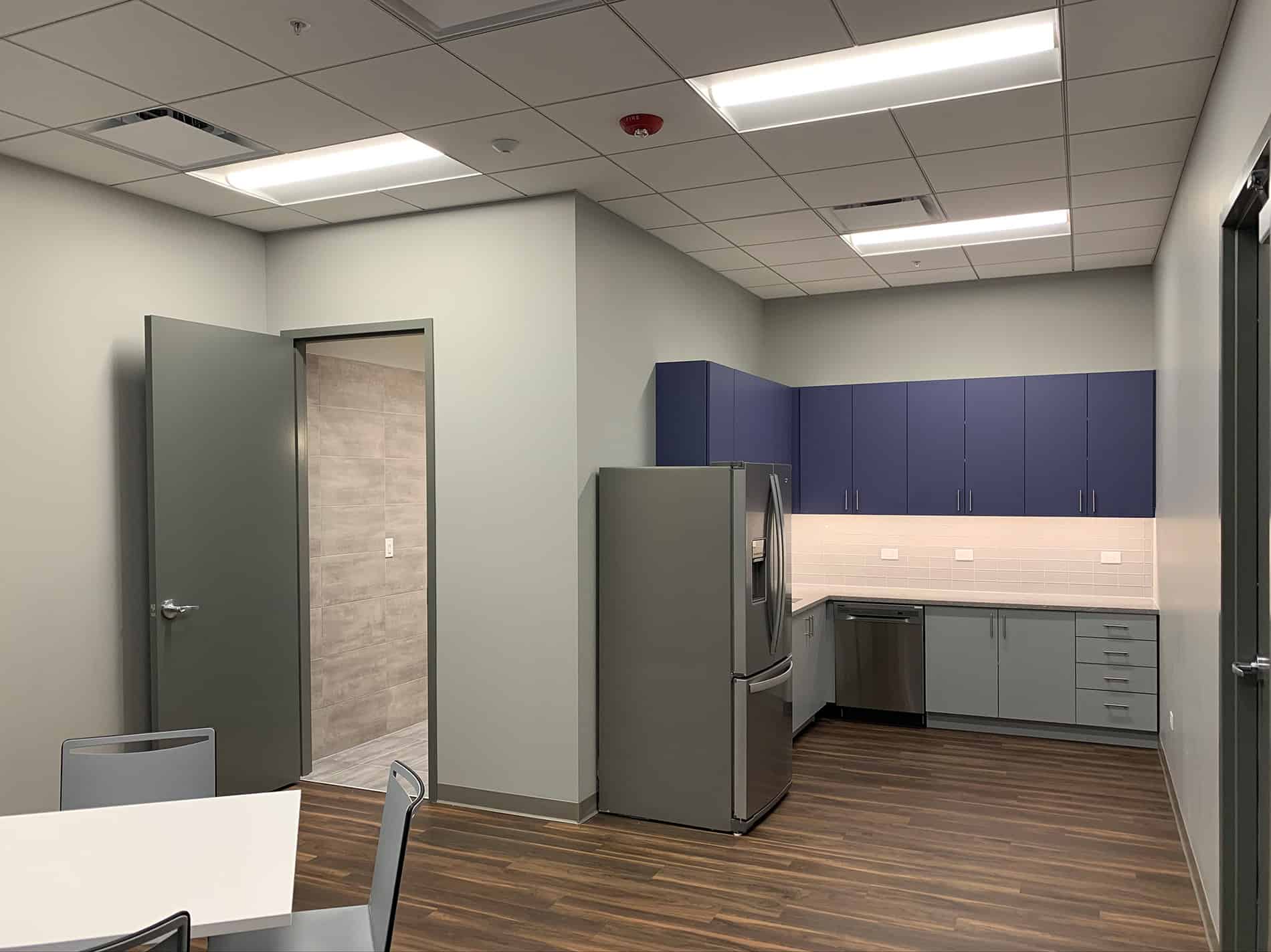 Part of an employee cafeteria in CODA’s newly renovated office space has a refrigerator, counter space, and a table with chairs.
